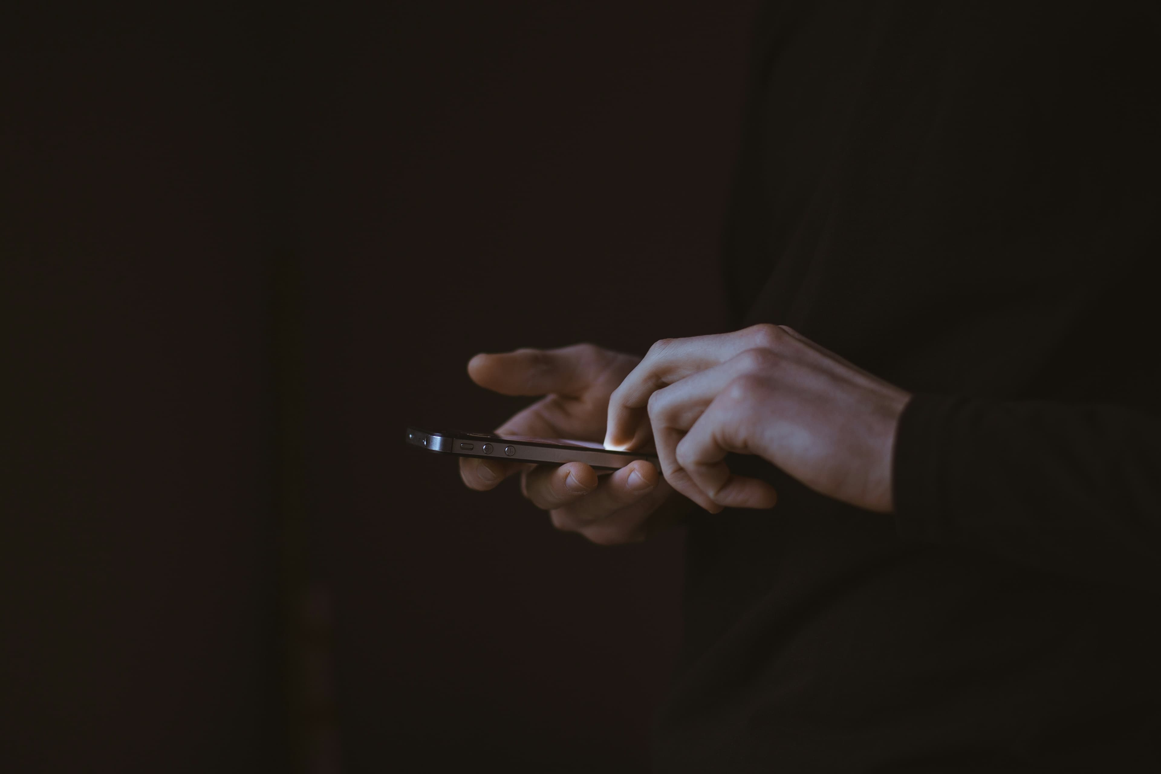 Hands holding a smartphone in low light, screen glow on fingers